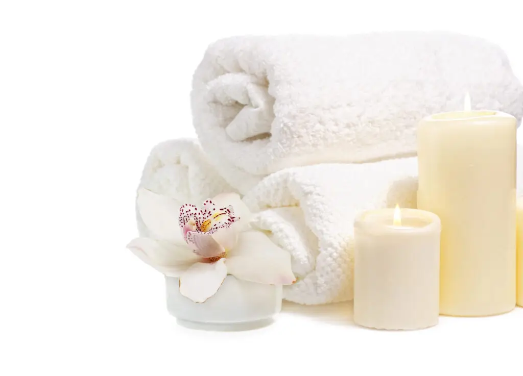 Opgerolde witte handdoeken met twee kaarsen en een witte orchidee op een witte achtergrond.