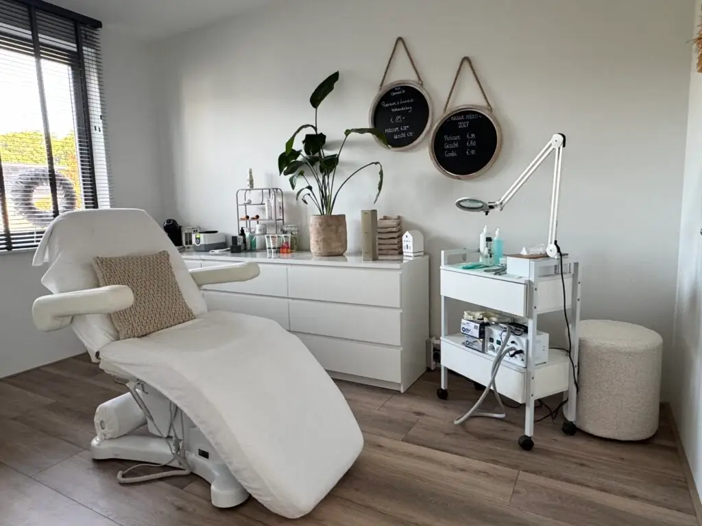 De salon met een witte behandelstoel, een witte kast, een grote plant en twee ronde zwarte bordjes aan de muur.